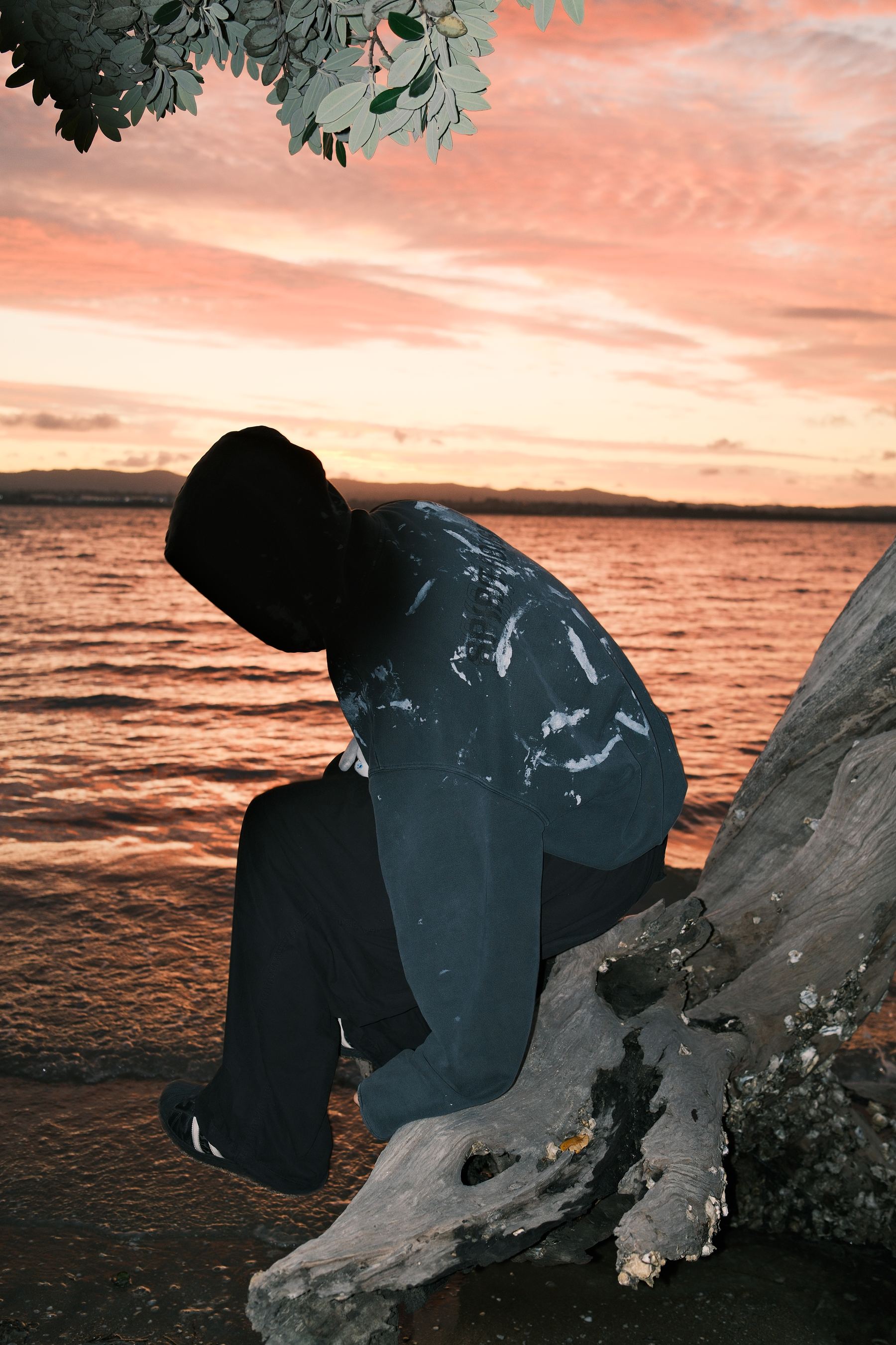 Spirit House campaign photograph — a figure seated on driftwood at the water's edge.